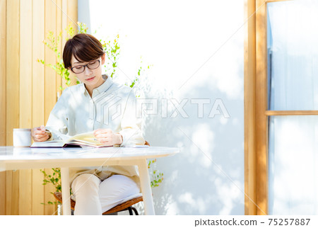Middle-aged woman with glasses reading on the terrace 75257887