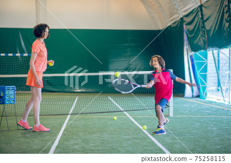 Female coach in bright clothes playing tennis with a boy 75258115
