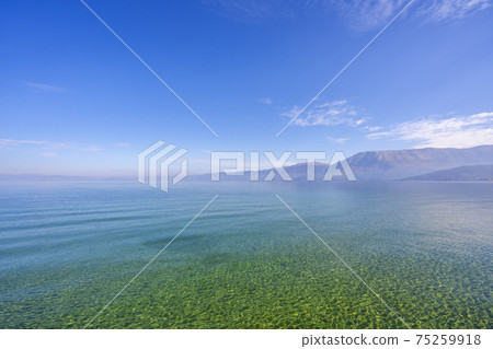 Amazing view on the green tree, mountains, sea with turquoise water and colorful blue sky at sunrise. Summer landscape in mountains on seashore. 75259918