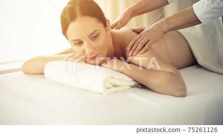 Pretty brunette woman enjoying procedure of back massage in spa salon. Beauty concept Pretty brunette woman enjoying procedure of back massage in spa salon. Beauty concept 75261126