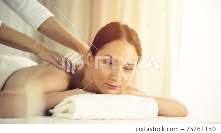 Pretty brunette woman enjoying procedure of back massage in spa salon. Beauty concept Pretty brunette woman enjoying procedure of back massage in spa salon. Beauty concept 75261130