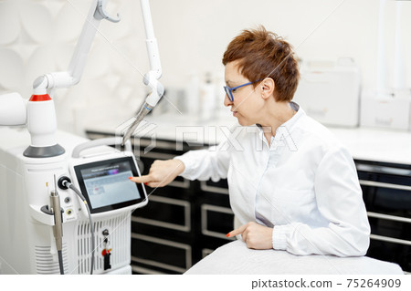 Cosmetologist near laser treatment device in beauty clinic. 75264909