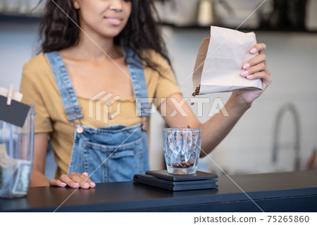 Female hand pouring coffee beans into measuring cup Female hand pouring coffee beans into measuring cup 75265860