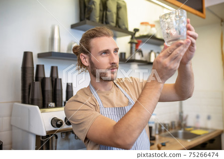 Attentive man looking at glass in raised hands 75266474