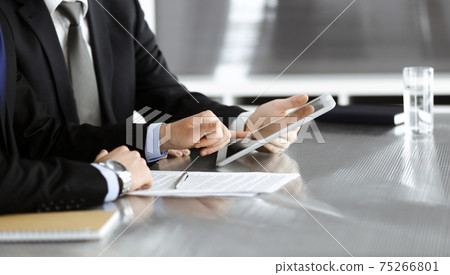 Unknown businessmen using tablet computer and work together at the glass desk in modern office, close-up. Teamwork and partnership concept Unknown businessmen using tablet computer and work together at the glass desk in modern office, close-up. Teamwork and partnership concept 75266801