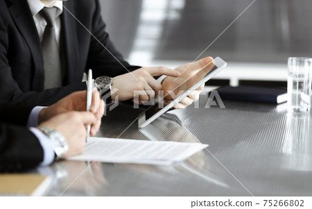 Unknown businessmen using tablet computer and work together at the glass desk in modern office, close-up. Teamwork and partnership concept 75266802