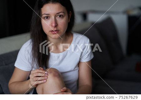 Portrait of beaten woman with tears of her face and bruise on knee sit on the sofa Portrait of beaten woman with tears of her face and bruise on knee sit on the sofa 75267629