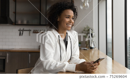 Close up smiling dreamy African American woman distracted from phone 75269604