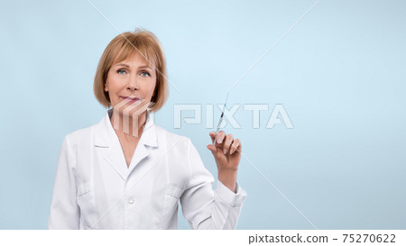 Senior female doctor with syringe looking at cmera on blue studio background, banner design with empty space Senior female doctor with syringe looking at cmera on blue studio background, banner design with empty space 75270622