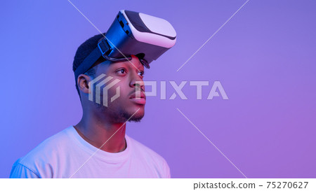 Handsome Black Man Wearing VR Glasses Looking Aside Over Purple Background Handsome Black Man Wearing VR Glasses Looking Aside Over Purple Background 75270627