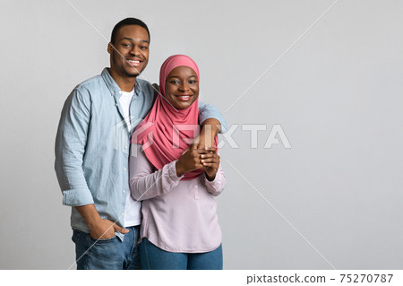 Cheerful loving african american muslim couple hugging on grey Cheerful loving african american muslim couple hugging on grey 75270787