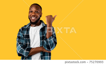 Cheerful Black Guy Pointing Thumb Aside Standing Over Yellow Background 75270993