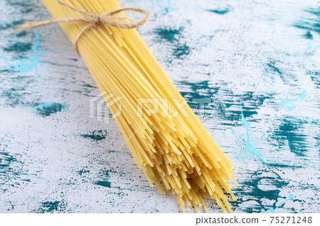 Uncooked spaghetti pasta tied with rope on colorful surface 75271248