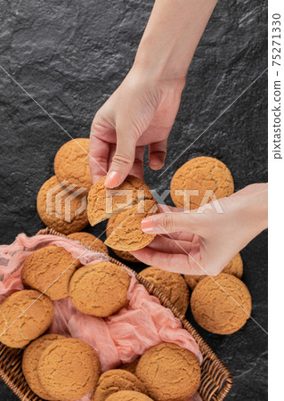 Cutting an oatmeal cookie in the hand into two pieces Cutting an oatmeal cookie in the hand into two pieces 75271330