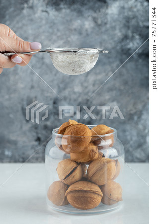 Female hand sprinkling a sugar powder on a walnut shaped cookies Female hand sprinkling a sugar powder on a walnut shaped cookies 75271344