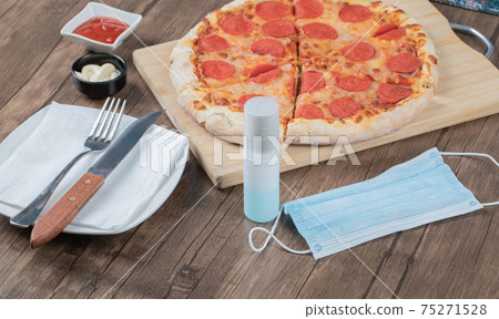 Pepperoni pizza on a wooden board with sauces, plate, hand sanitizer 75271528