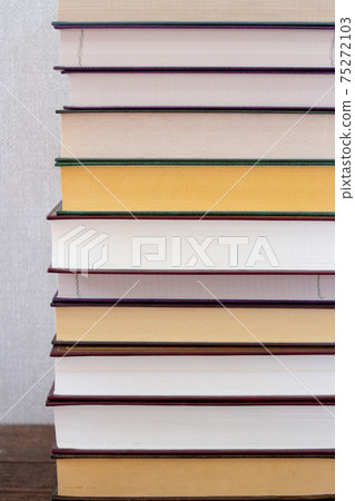 A vertical of stack of books on a wooden shelf and a gray background A vertical of stack of books on a wooden shelf and a gray background 75272103