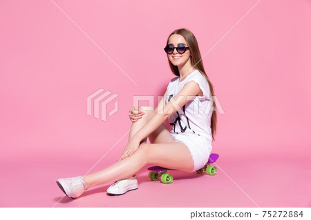 Cheerful young girl with a skateboard on the pink background 75272884