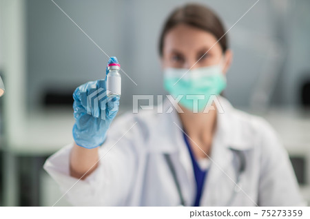 A young female lab technician wearing a medical mask shows off a coronavirus vaccine in her lab at the hospital 75273359