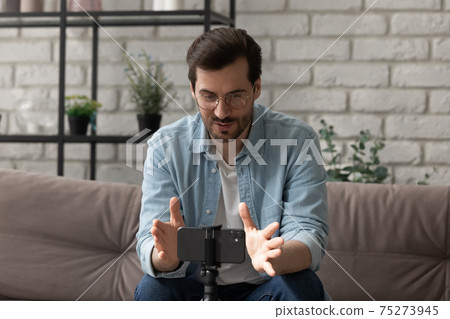 Confident male coach sit on sofa before smartphone record training 75273945