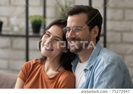 Young loving couple relaxing at home hugging looking away dreaming Young loving couple relaxing at home hugging looking away dreaming 75273947