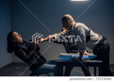 A bad cop threatens a suspect with a gun at a police station in the presence of a lawyer. A bad cop threatens a suspect with a gun at a police station in the presence of a lawyer. 75274088