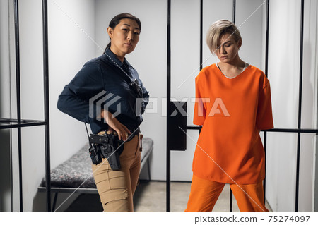 Shooting a movie about a women's prison. Backstage. Asian warden and a criminal girl in a yellow robe on the background of a prison cell. Shooting a movie about a women's prison. Backstage. Asian warden and a criminal girl in a yellow robe on the background of a prison cell. 75274097