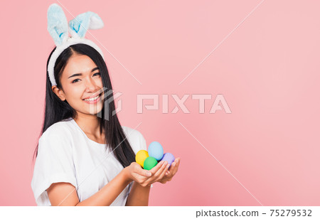 woman smiling wearing rabbit ears holding colorful Easter eggs gift on hands woman smiling wearing rabbit ears holding colorful Easter eggs gift on hands 75279532