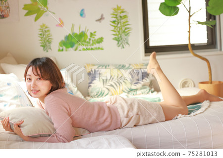 A woman holding a cushion and lying down with a smile 75281013