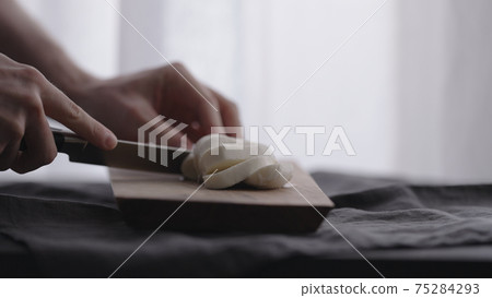 man slicing mozzarella ball on olive wood board with window on background 75284293