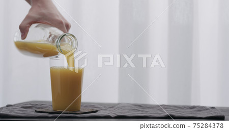 man hand pour orange juice from glass bottle to tumbler glass on black wood table 75284378