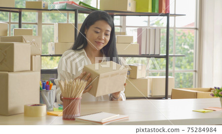 Asian business woman packing postal parcel packaging carton box delivery, working from home, selling products online business. Shipping service. People lifestyle in coronavirus pandemic. SME ecommerce Asian business woman packing postal parcel packaging carton box delivery, working from home, selling products online business. Shipping service. People lifestyle in coronavirus pandemic. SME ecommerce 75284984