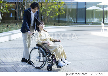 A woman in a wheelchair and a man helping 75287718