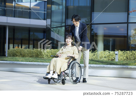 一個坐在輪椅上的女人和一個男人幫助 75287723
