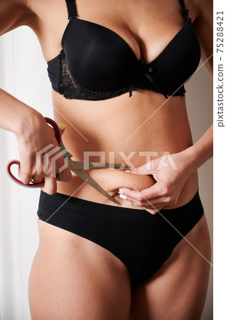 Young woman cutting off excess fat with scissors. 75288421