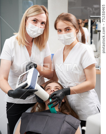 Dentist and assistant examining patient teeth with dental x-ray machine. 75288465