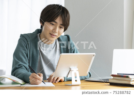 Image of a young man studying while looking at a tablet, a student taking an online class 75288782