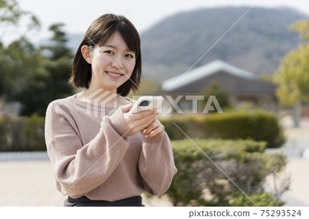 A woman using a smartphone in a park A woman using a smartphone in a park 75293524