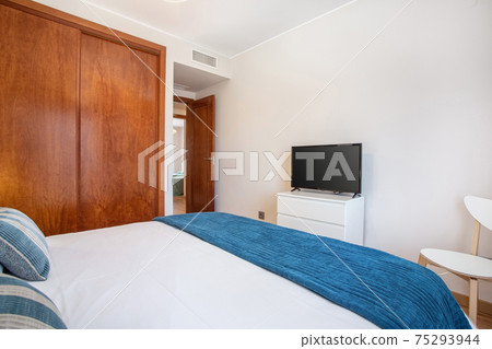 Shot from corner of bedroom, view from bed to a tv on a stand, a wardrobe on the side and an open door showing another room. 75293944