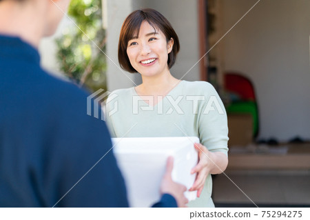 Woman receiving parcel from delivery staff 75294275