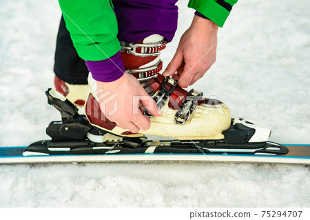 The skier wears footwear for skiing and fixes the fastener The skier wears footwear for skiing and fixes the fastener 75294707