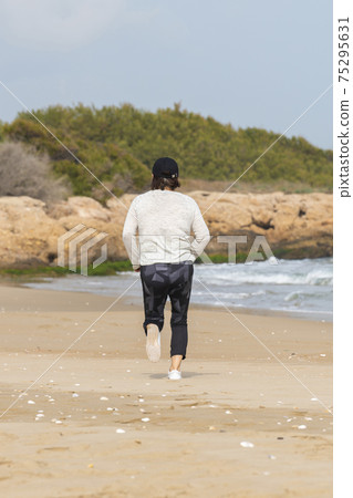 Mature woman with a cap running at the beach Mature woman with a cap running at the beach 75295631