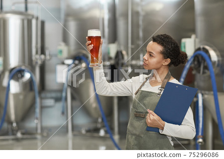 Young Woman Looking at Beer Glass at Brewery 75296086