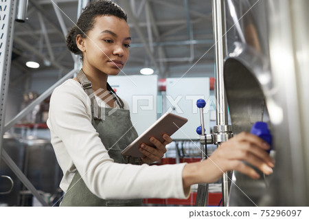 Young Female Worker Opening Valve at Factory 75296097