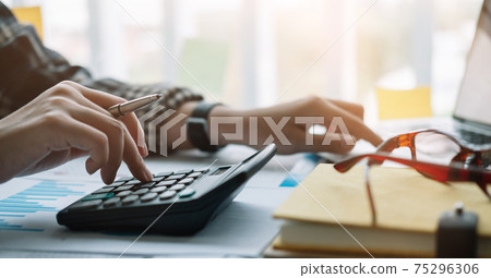 Close up hand man doing finance and calculate with calculator on desk about cost , work from home concept Close up hand man doing finance and calculate with calculator on desk about cost , work from home concept 75296306