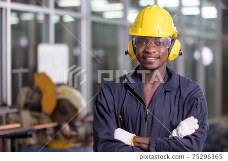 Portrait of cheerful black worker wearing protective headphones posing looking at camera and enjoying work at background factory Portrait of cheerful black worker wearing protective headphones posing looking at camera and enjoying work at background factory 75296365