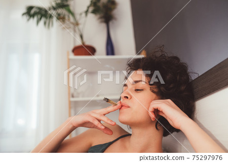 Woman laying on her bed and smoking her hand-rolled cigarette 75297976