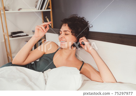 Girl laying at the bed and enjoying her day at the morning with cigarette 75297977