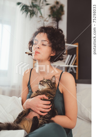 Woman smoking hand-rolled cigarette while holding her cat 75298033