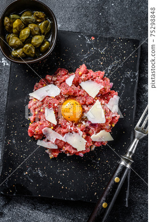 Tartar beef with a quail egg, capers and Parmesan cheese. Black background. Top view Tartar beef with a quail egg, capers and Parmesan cheese. Black background. Top view 75298848